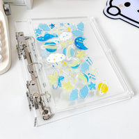 A transparent A5 acrylic binder with with blue and yellow charms shapes like stars, clouds, moon, etc.