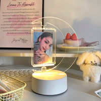 A moon-shaped spinning photocard display with a light-up base, showcasing a photo within its clear acrylic frame.